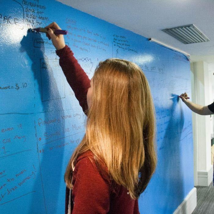 A woman and a man working together, writing on a whiteboard clear paint wall