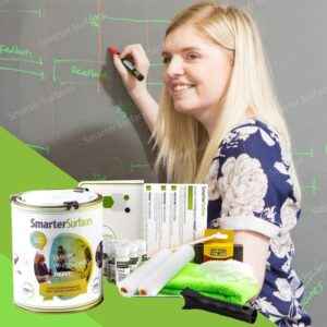 A woman is writing on a whiteboard-painted wall with a product kit in front of her.